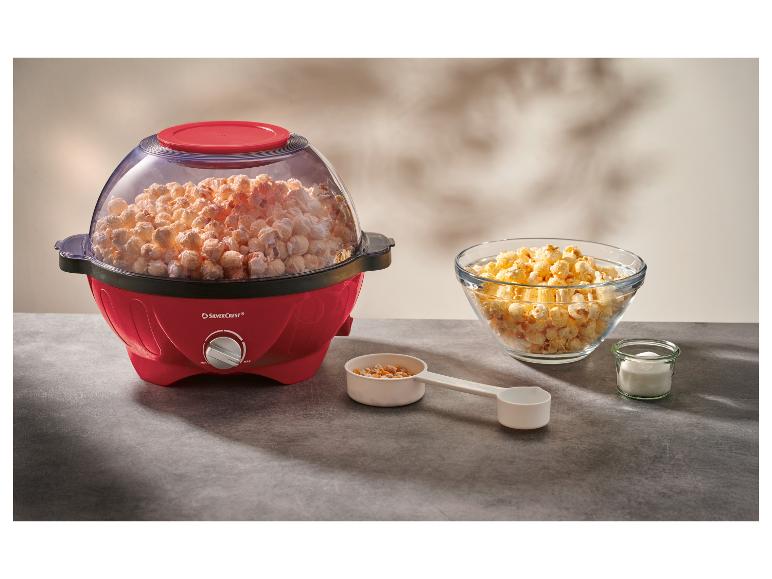 Roter Popcorn-Maker voller Popcorn, mit einer Schüssel Popcorn und Zutaten auf dem Tisch.