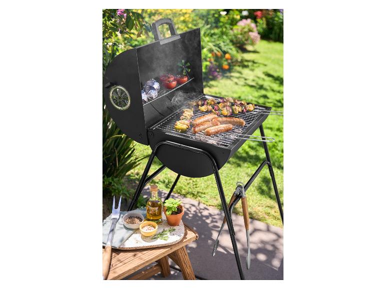 Holzkohlegrill mit Würstchen und Spießen in einem sonnigen Garten.