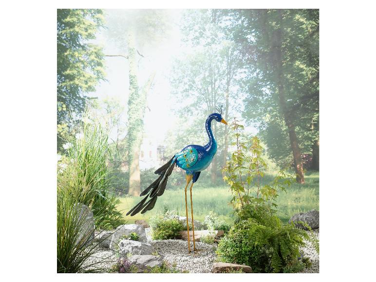 Eine Metallskulptur eines Pfaus in einer Gartenlandschaft.