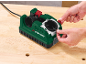 Bohrer- und Messerschärfer mit grünem Gehäuse, von Händen auf einem Holztisch bedient.