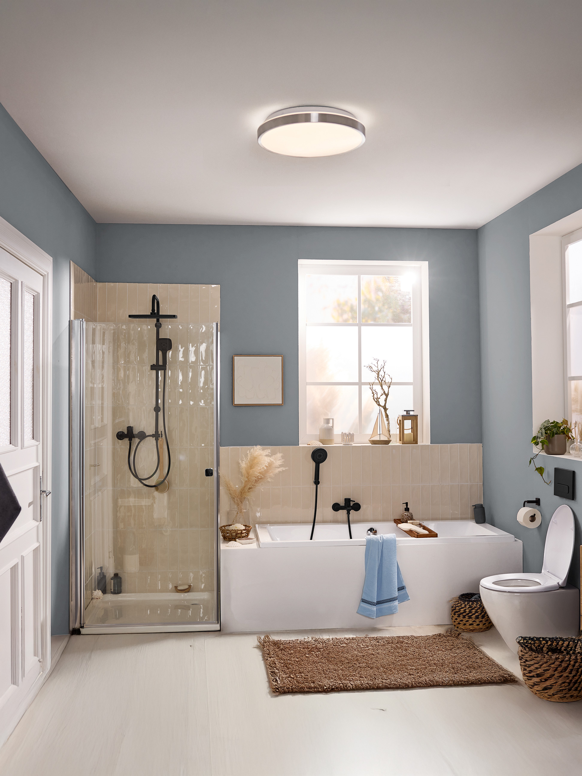 Modernes Badezimmer mit blauen Wänden, Duschkabine, Badewanne, Toilette und runder Deckenleuchte.