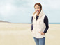 Eine Frau trägt eine weiße Steppweste mit Kapuze am Strand.