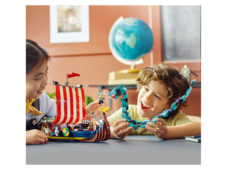 Zwei Kinder spielen mit LEGO-Sets, einem Wikingerschiff und einem blauen Drachen.