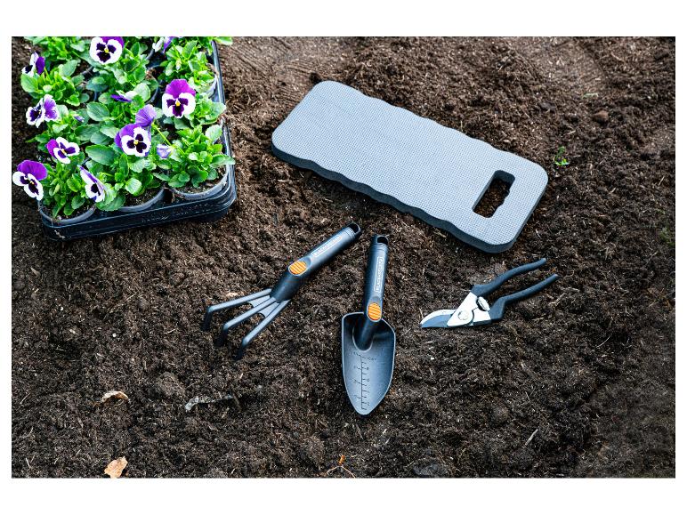 Stiefmütterchen-Pflanzen, Gartengeräte und Kniekissen auf der Erde.