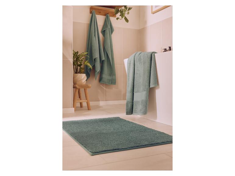 Badezimmer mit grünen Handtüchern und Teppich, Pflanze und Holzschemel.