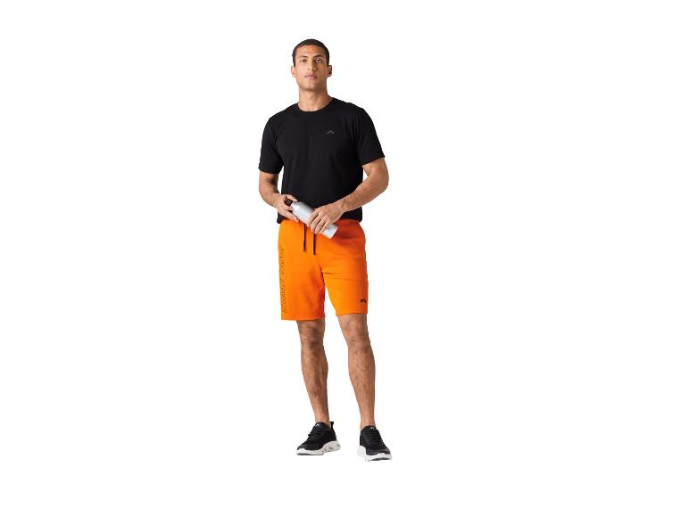 Mann in schwarzem T-Shirt und orangenen Shorts, hält eine Wasserflasche.