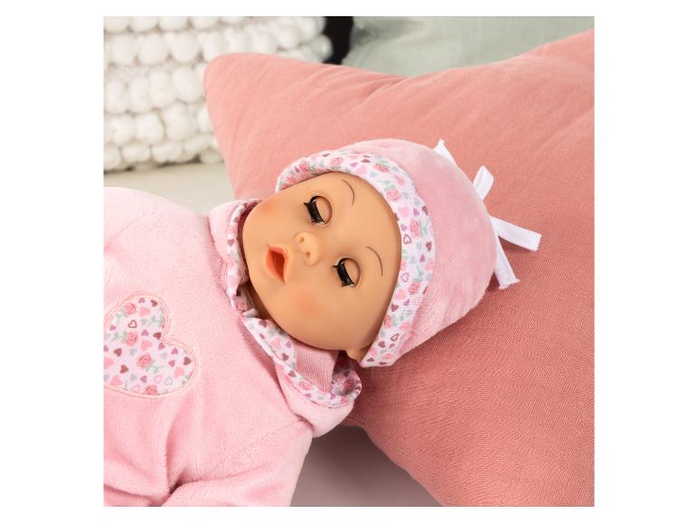 Eine Puppe in rosa Schlafanzug und Mütze mit Herzen und Rosen, liegend auf einem rosa Kissen.