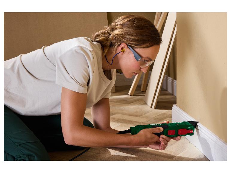 Eine Frau benutzt ein grünes und rotes Multifunktionswerkzeug, um eine weiße Fußleiste zu schneiden.