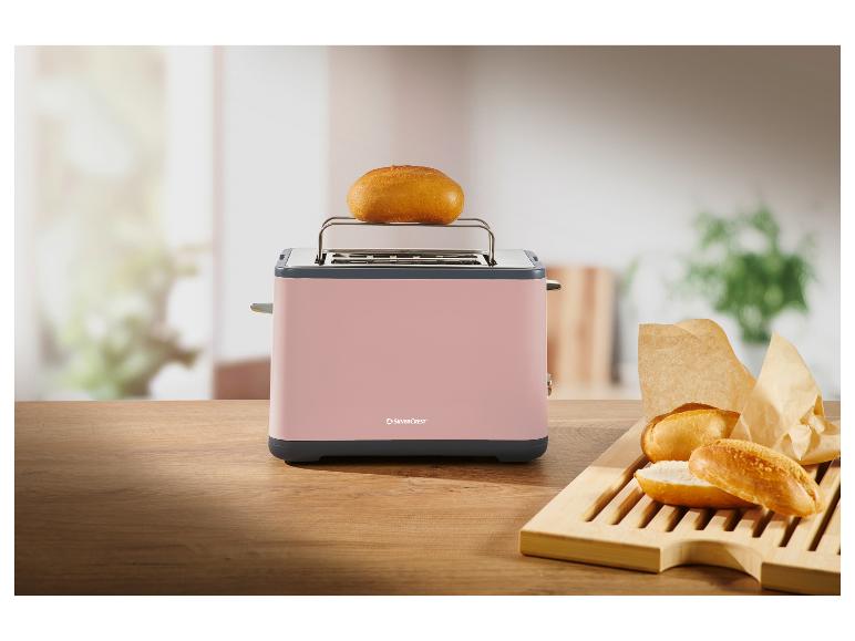 Rosa Toaster mit Brötchen auf einem Holztisch, ein Brötchen oben auf dem Toaster.