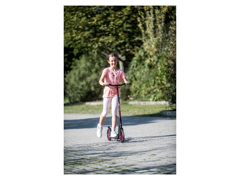 Lächelndes Mädchen in rosa T-Shirt und weißer Caprihose, fährt einen schwarz-rosa Roller.