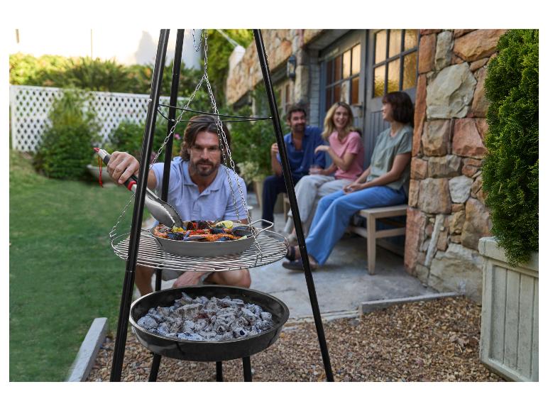Mann grillt Meeresfrüchte auf einem Dreibein-Grill mit Freunden im Hintergrund.