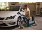 Ein Mann poliert ein weißes Auto mit einer Rotationspoliermaschine in einer Garage.