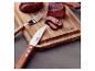 Gegrilltes Fleisch auf einem Holzschneidebrett mit Gabel und Messer, gewürzt mit Salz und Pfeffer.