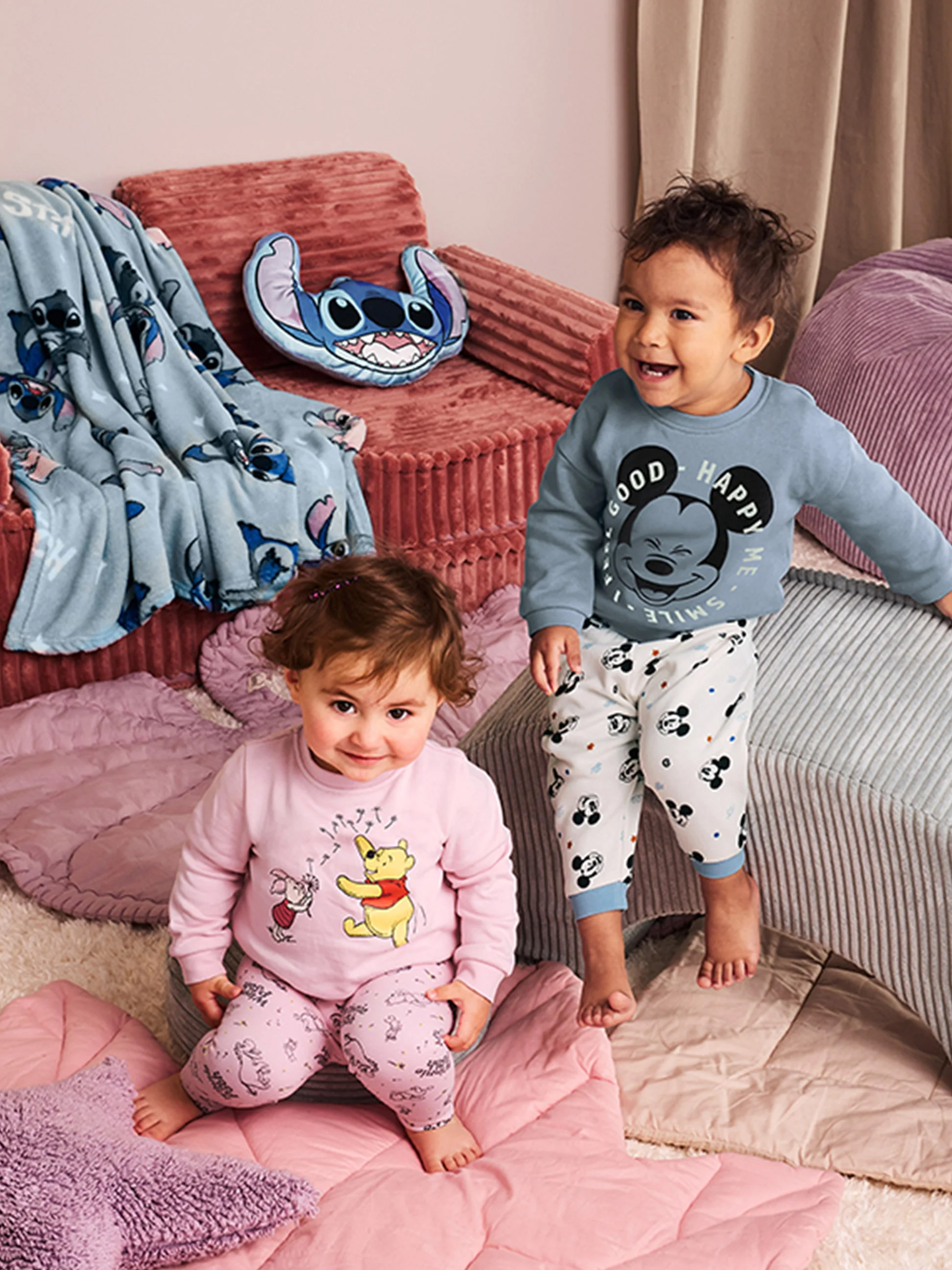 Zwei Babys in Disney-Pyjamas, umgeben von Stitch-Decken und Kissen.