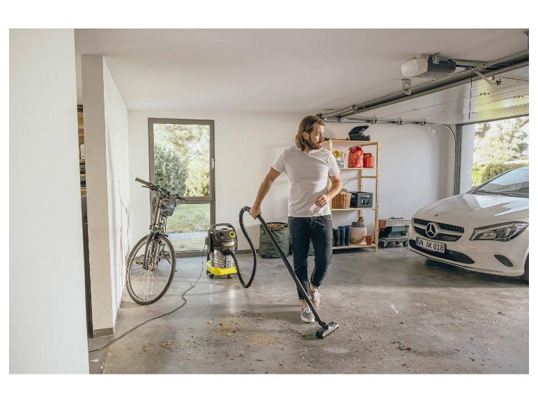 Mann saugt Garage mit einem Nass-Trockensauger, mit Fahrrad und Auto im Hintergrund.