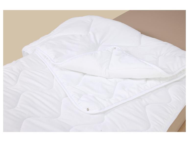 Weiße Steppdecke mit Druckknöpfen auf einem hellbraunen Bett.