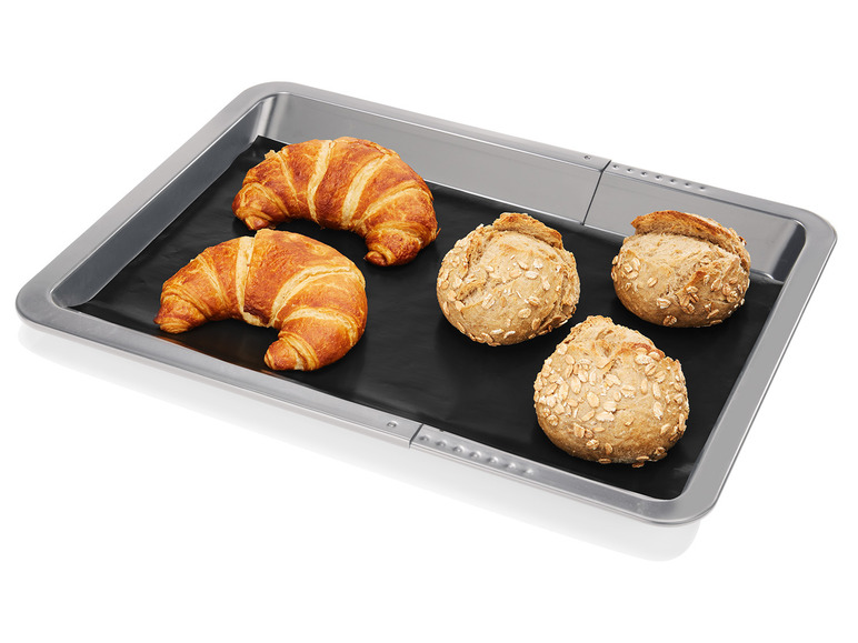 Zwei Croissants und drei Brötchen auf einem Backblech mit Backpapier.