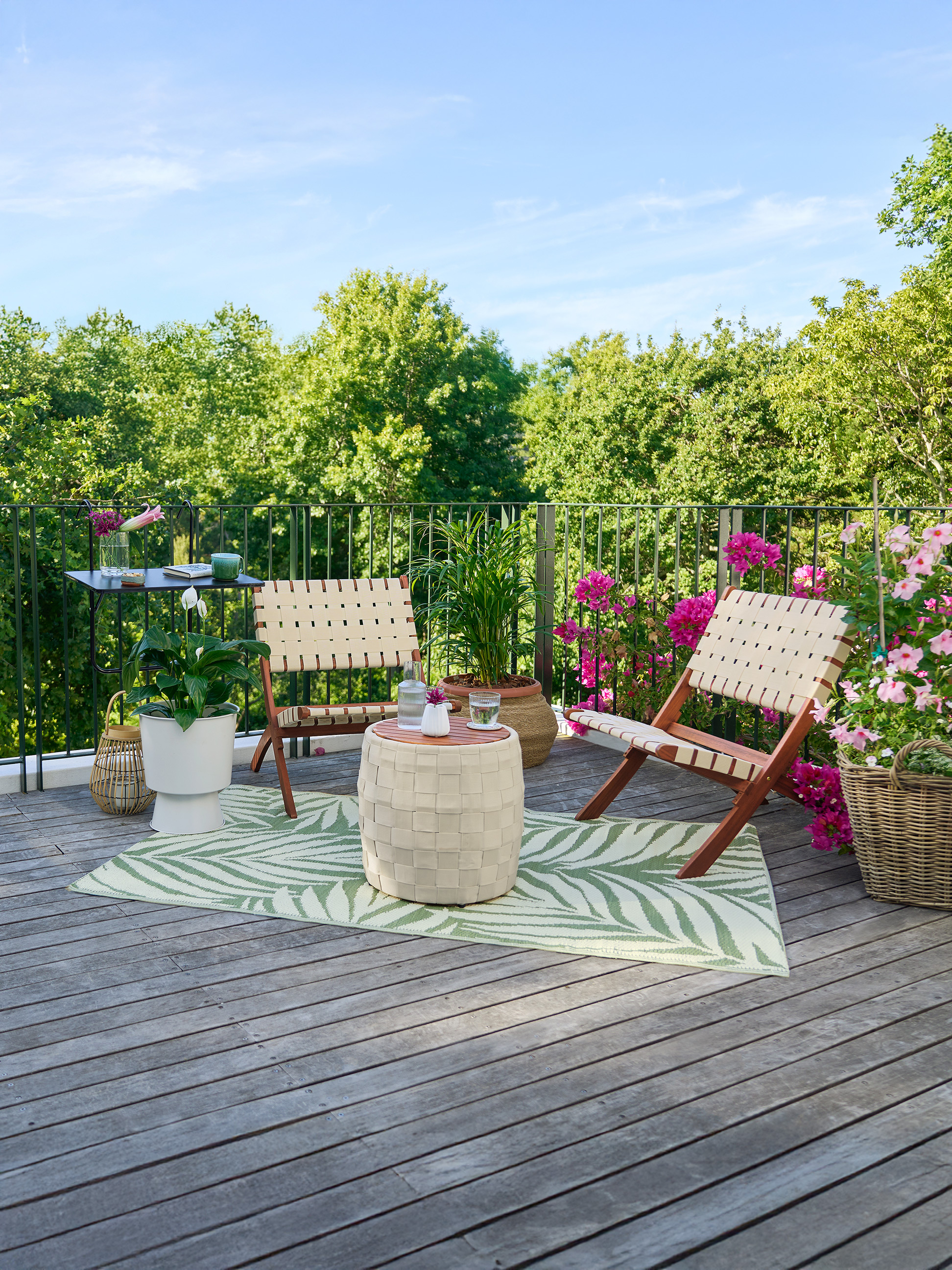 Balkon mit zwei Stühlen, einem Tisch, einem Teppich und Blumen.