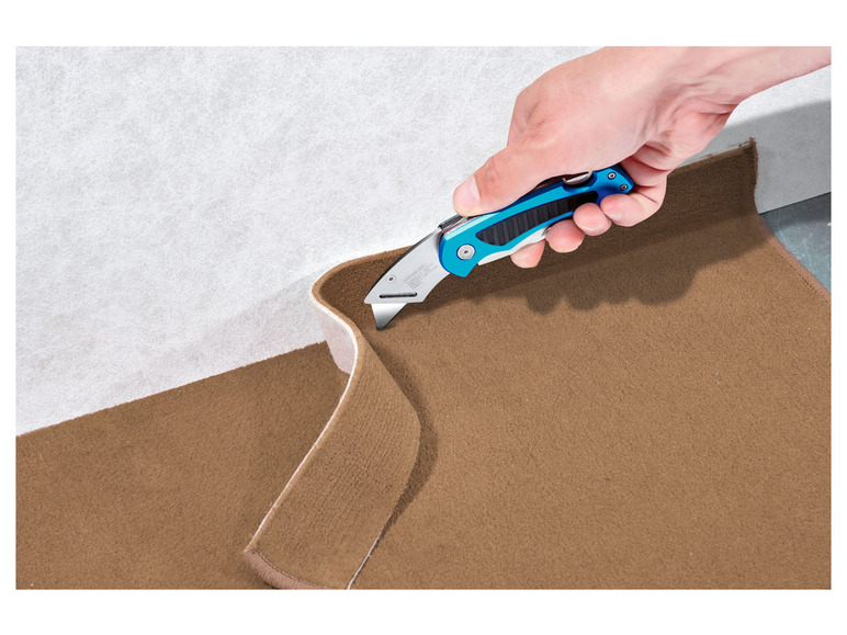 Eine Hand schneidet mit einem Messer einen Teppich.