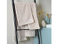 Beige Handtücher hängen an einem schwarzen Leiterregal in einem Badezimmer mit hellblauen Akzenten.