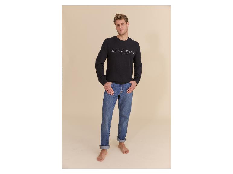 Mann in schwarzem Pullover mit Logo und blauen Jeans, barfuß.