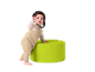 Baby im beigen Strampler steht neben einem grünen Pouf.