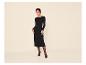 Frau in einem schwarzen langärmeligen Midikleid, schwarzer Strumpfhose und schwarzen Absätzen.
