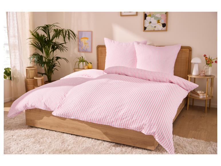 Rosa gestreifte Bettwäsche auf einem Holzbett in einem Schlafzimmer mit Pflanzen und Bildern.