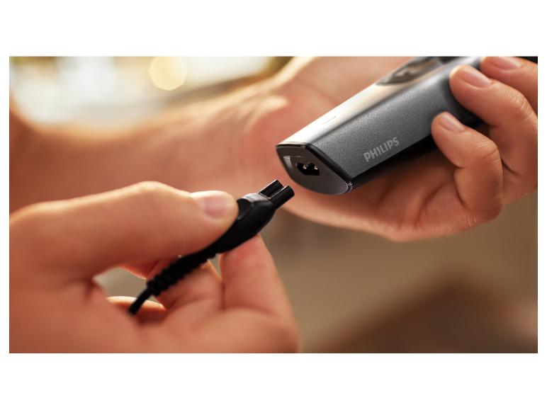 Hände schließen ein Ladegerät an einen grauen Elektrorasierer an.