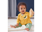Ein Baby in einem gelben Pullover und grünen Hosen mit einem Vogelmotiv.