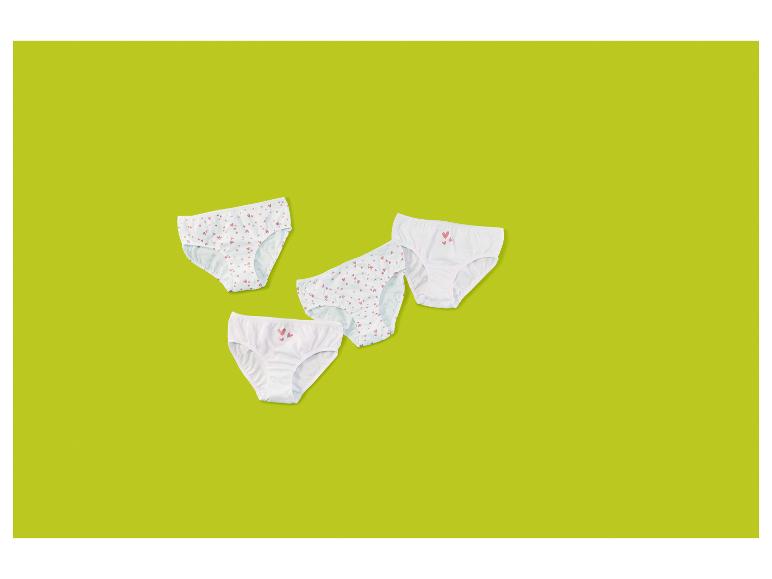 Vier weiße Kinderunterhosen, zwei mit Herzmustern, auf grünem Hintergrund.