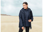 Eine Frau trägt eine dunkelblaue Parka mit einer gefütterten Innenjacke am Strand.
