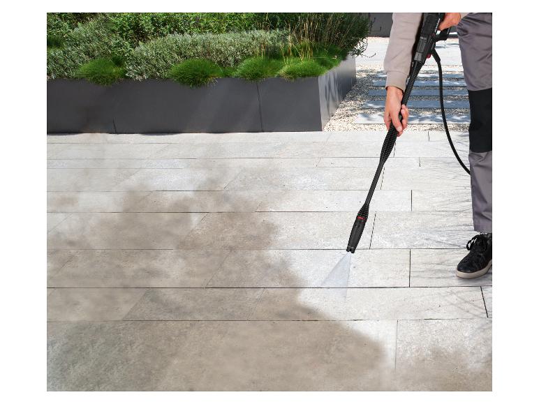 Person reinigt Terrasse mit Hochdruckreiniger, entfernt Schmutz von hellen Fliesen.