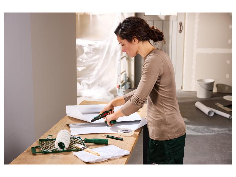 Frau schneidet Tapete mit einem Cutter, Malutensilien auf dem Tisch.