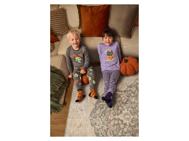 Zwei Kinder in gemütlichen Halloween-Pyjamas sitzen auf dem Boden vor einem Sofa