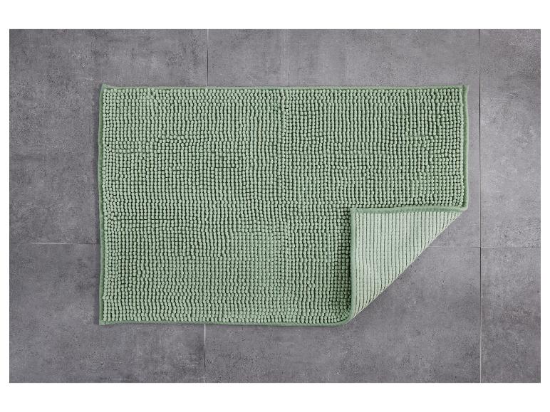 Eine grüne Badematte mit Textur auf einem grauen Fliesenboden.