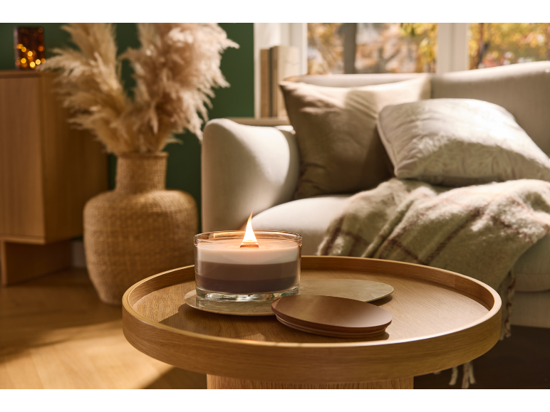 Eine brennende Schichtkerze auf einem Holznebentisch in einem gemütlichen Wohnzimmer mit Sofa.
