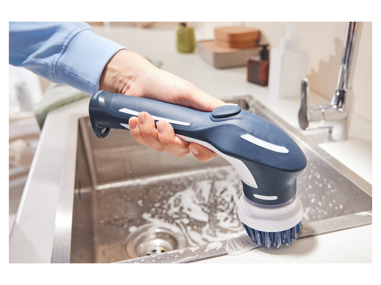 Eine Hand hält eine blaue und weiße Bürste, die ein Waschbecken reinigt.