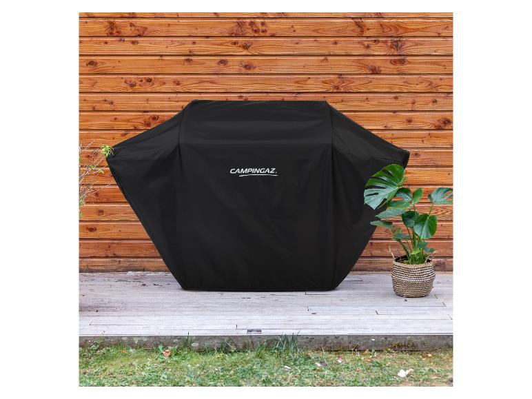 Schwarze Grillabdeckung auf einer Holzterrasse mit Holzwand im Hintergrund und Pflanzen.