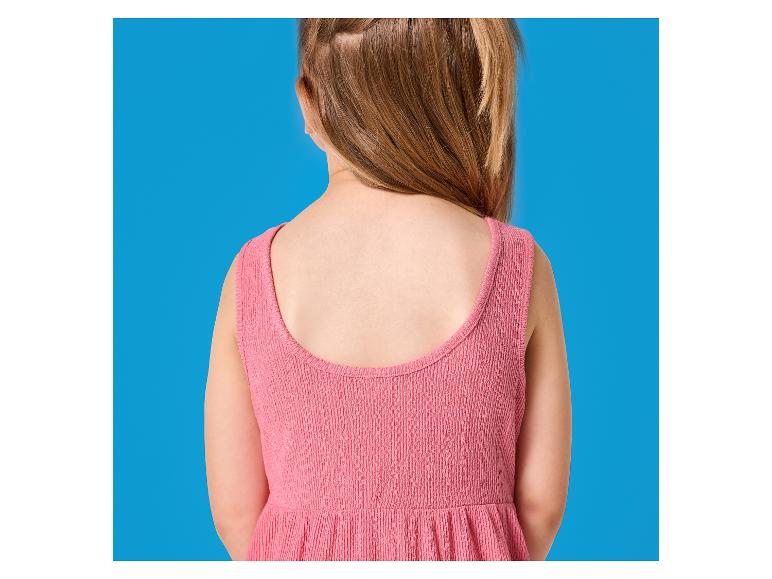 Rückenansicht eines Kindes in einem rosa Kleid vor blauem Hintergrund.