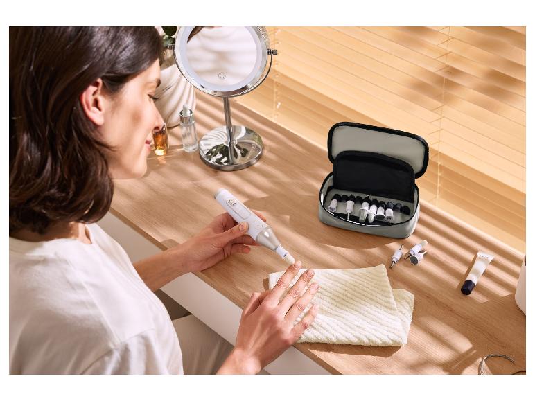 Frau benutzt elektrische Nagelfeile mit Maniküre-Set auf Holztisch.