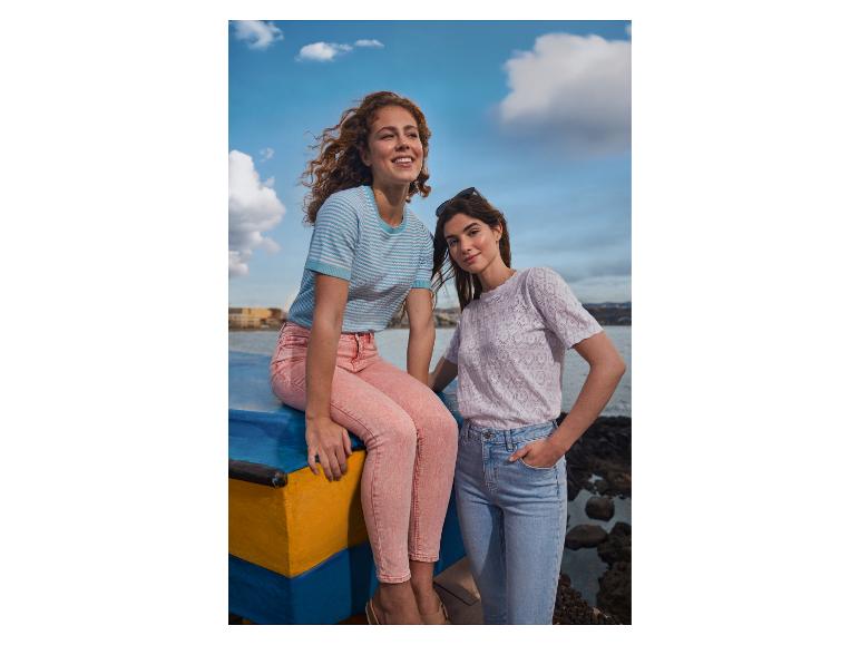 Zwei Frauen in Jeans und T-Shirts am Wasser, eine sitzt auf einem Boot.