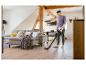 Mann saugt hellen Holzboden mit einem Akku-Staubsauger in einem modernen Wohnzimmer.