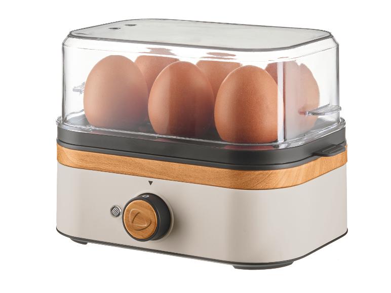 Eierkocher mit transparentem Deckel, sechs braunen Eiern und Holzoptik-Basis.