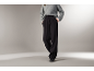 Frau in grauem Pullover und schwarzer, weiter Hose.