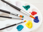 Eine Palette mit Farben und Pinseln, darunter blaue, gelbe, grüne und rote Farbe.