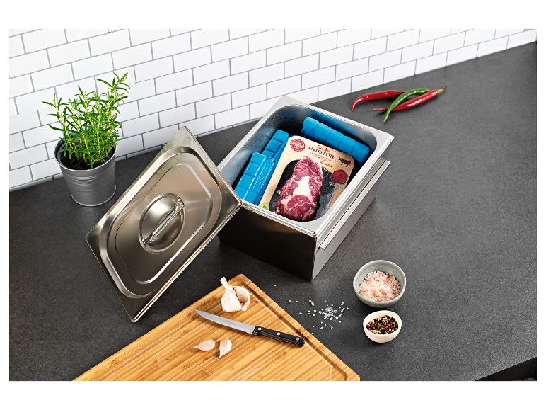 Edelstahl-Kühlbox mit frischem Entrecôte-Steak, Kühlakkus und Kochzutaten auf einer Küchenarbeitsplatte.