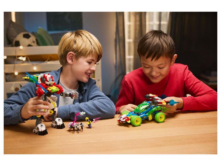 Zwei Jungen spielen mit LEGO-Sets, einem Roboter und einem Rennwagen, an einem Holztisch.