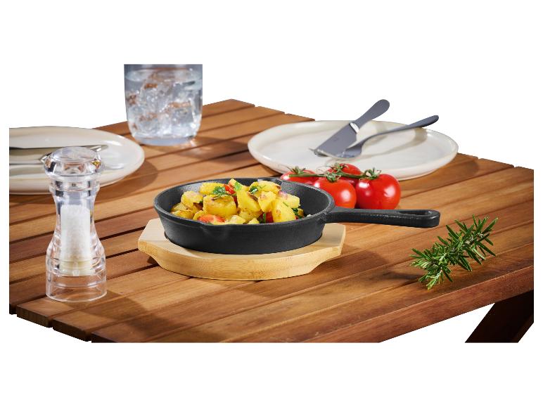 Gusseisenpfanne mit Bratkartoffeln, Salz, Tomaten und Rosmarin auf einem Holztisch.
