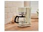 Cremefarbene Filterkaffeemaschine mit Kanne, Milch und Keksen auf einer Holztheke.